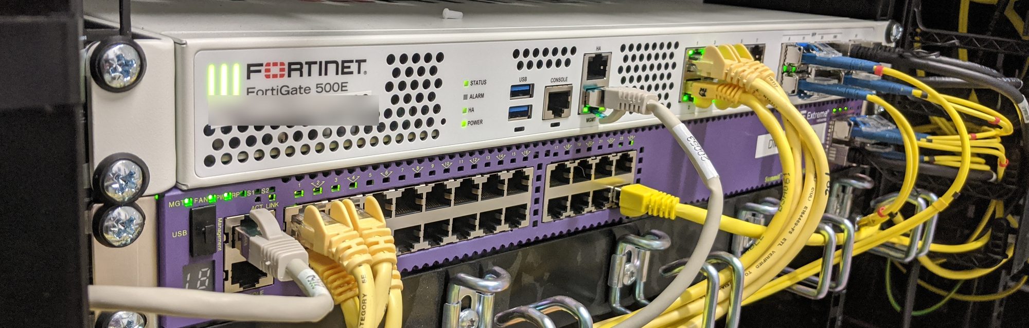 FortiGate-500E-Firewall im Rack, darunter ein Extreme-Networks-Switch mit gesteckten Netzwerkkabeln