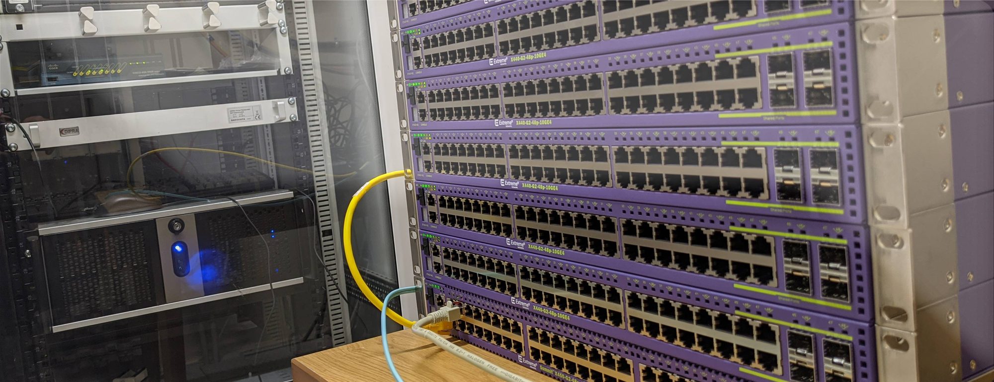Stapel aus sechs Extreme-Networks-Switches vom Typ X440-G2 im Serverschrank, daneben ein zweiter Schrank mit weiterer Technik
